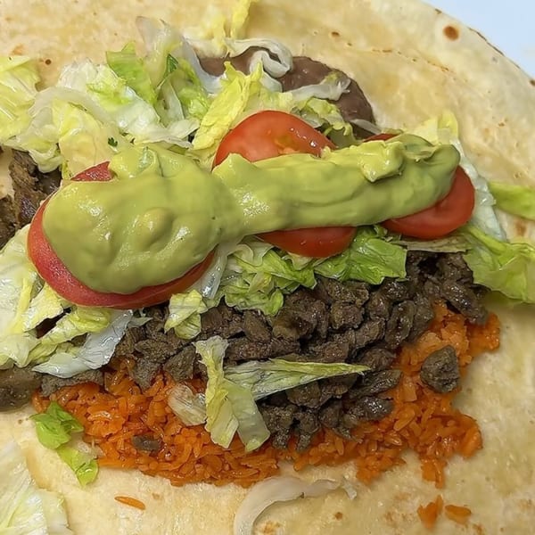 A large, open Taquería El Mundo burrito filled with steak, rice, lettuce, tomatoes, and guacamole.