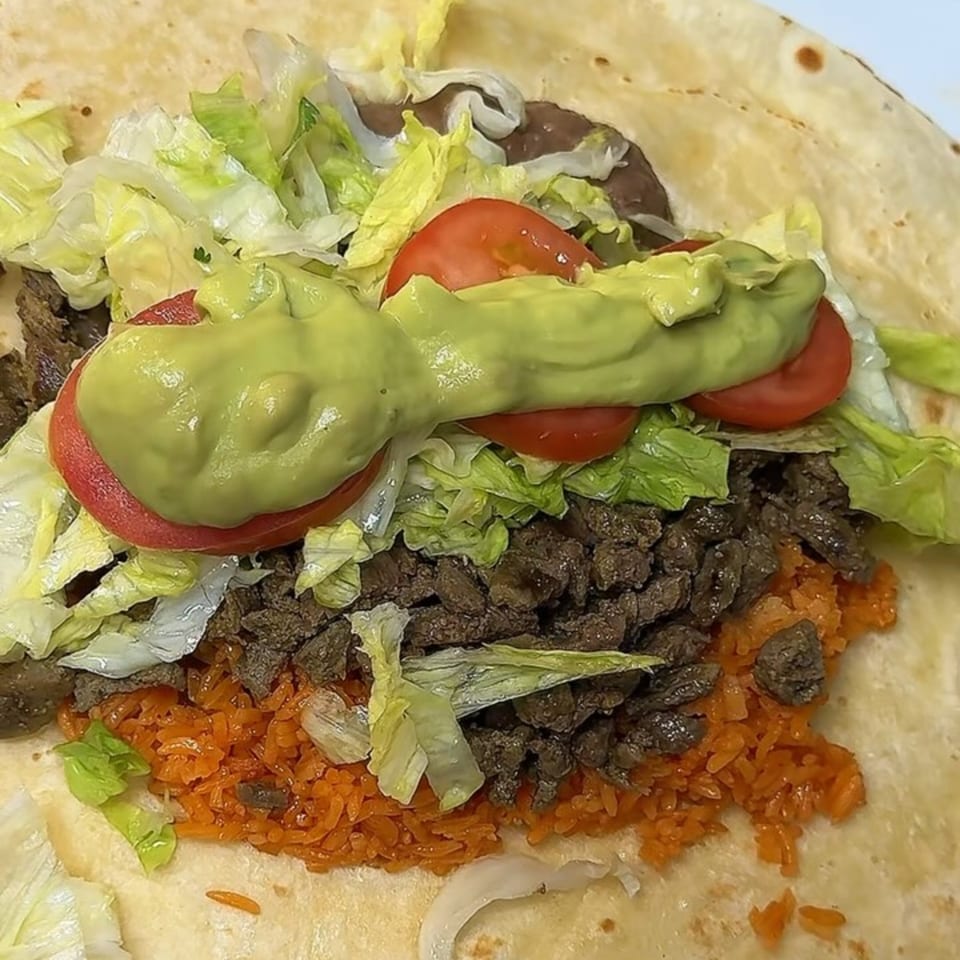 A large Taquería El Mundo burrito filled with meat, rice, lettuce, tomatoes, and guacamole.