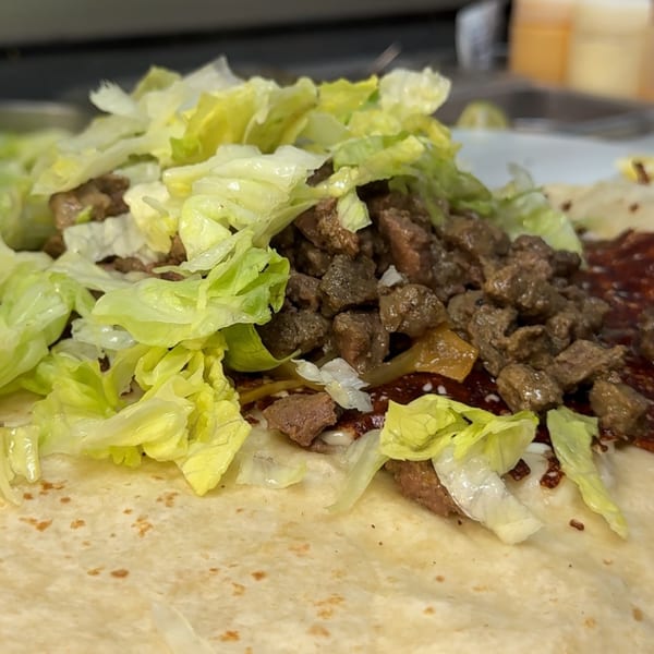 Close-up of a Taquería El Mundo burrito with diced meat, red sauce, and shredded lettuce.