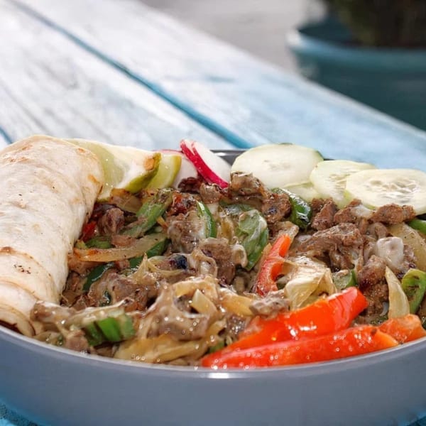 Mexican fajita bowl with steak, peppers, onions, and tortillas on a blue wooden table.
