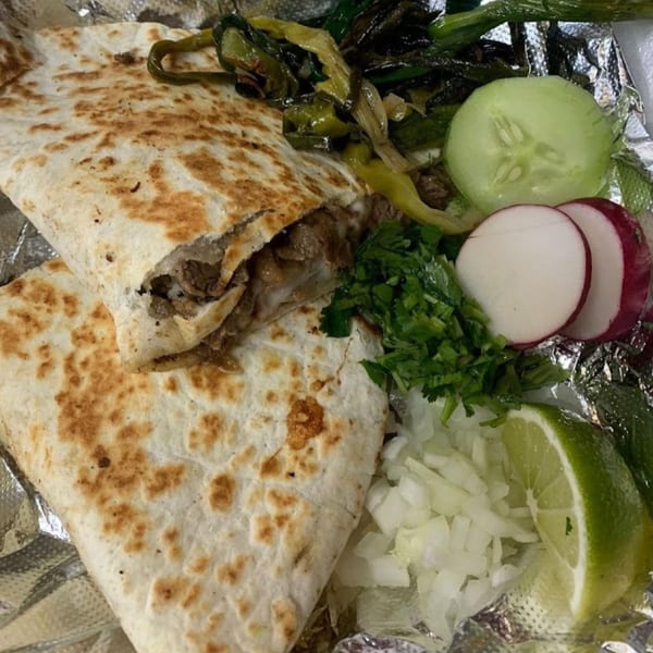 A Mexican quesadilla with meat and cheese, served with grilled peppers, cucumber, radishes, cilantro, onions, and lime.