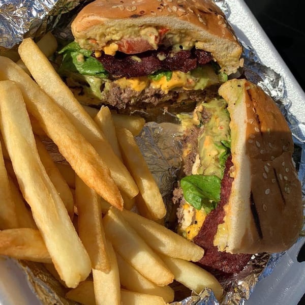 A cut-in-half burger with avocado, cheese, and bacon, served with a side of golden fries.