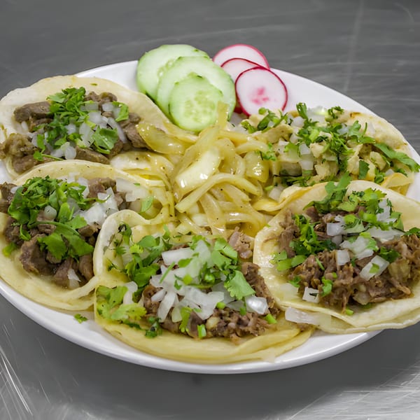 A plate of Taquería El Mundo's Mexican tacos with meat, onions, cilantro, and a side of cucumbers and radishes.
