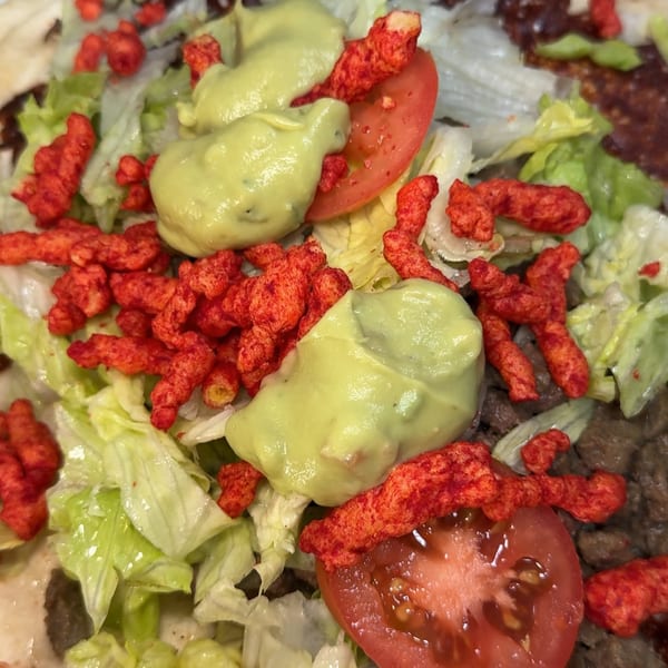 Mexican dish with ground meat, lettuce, tomato, guacamole, and red crunchy snacks.