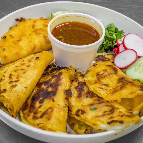 A plate of golden-brown quesabirria tacos with a side of consommé, radishes, and cilantro.