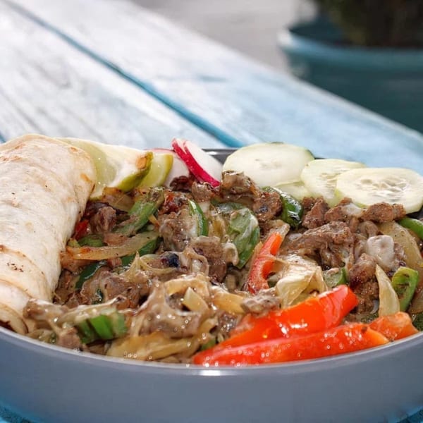 A close-up of a Mexican dish with beef, peppers, onions, and a tortilla on a blue table.