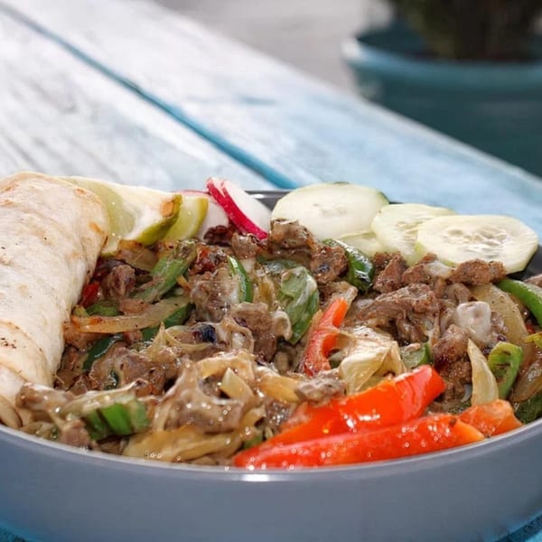 A bowl of Taquería El Mundo's Mexican fajitas with meat, peppers, onions, and a tortilla.