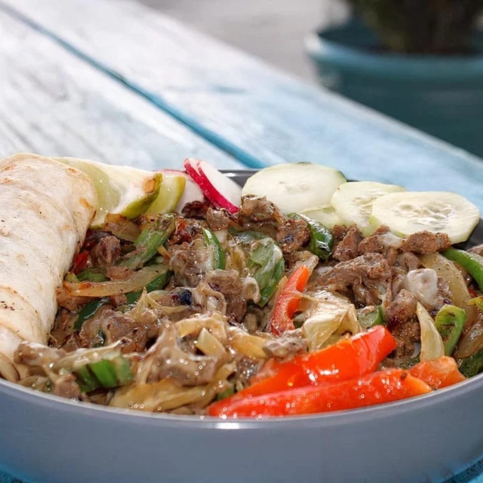 A bowl of Taquería El Mundo's Mexican fajitas with meat, peppers, onions, and a tortilla.