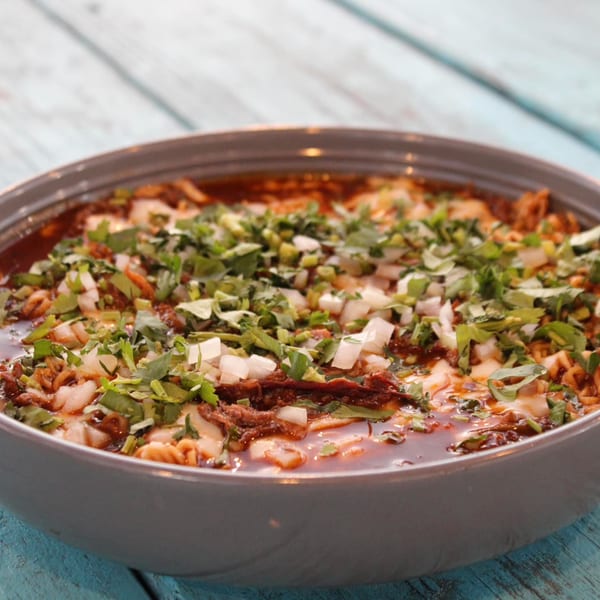 A close-up of a bowl of birria ramen from Taquería El Mundo, garnished with cilantro and diced onions.